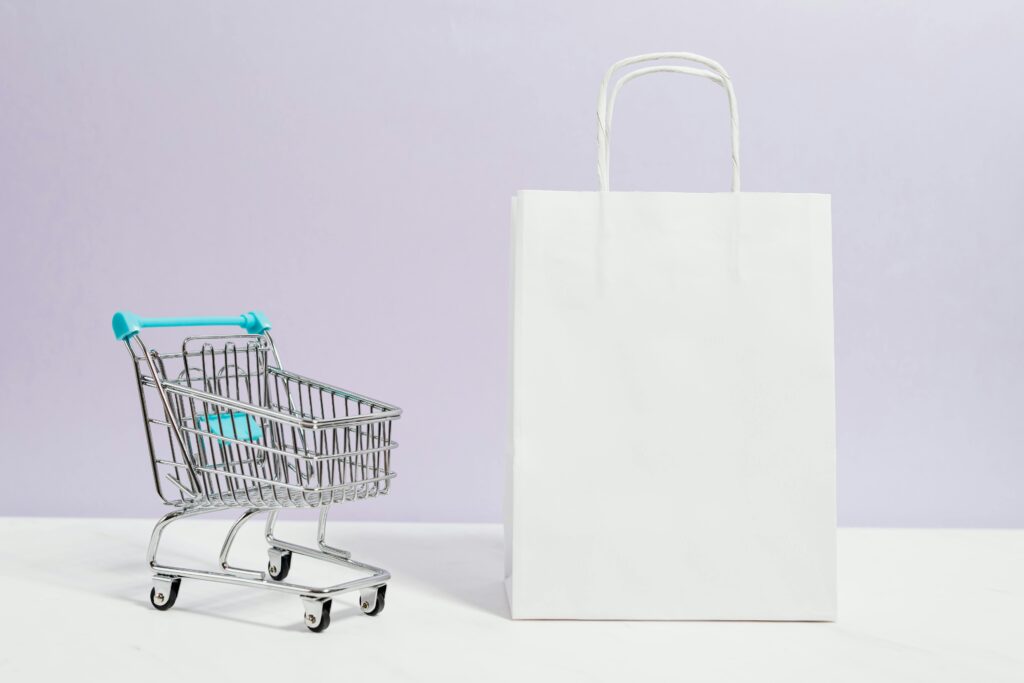 Minimalist image of a white shopping bag and mini cart on a soft pastel background. Ecommerce icons representing online shopping, showing that even if you don’t have Labubu, you can still sell online without being tired of chasing algorithms.