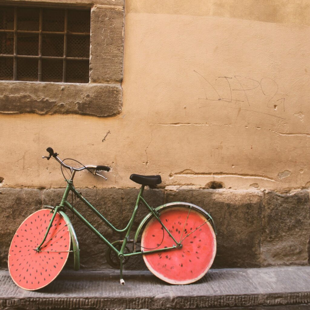A green bicycle with watermelon-themed wheels against a rustic stone wall in Arad, Romania.