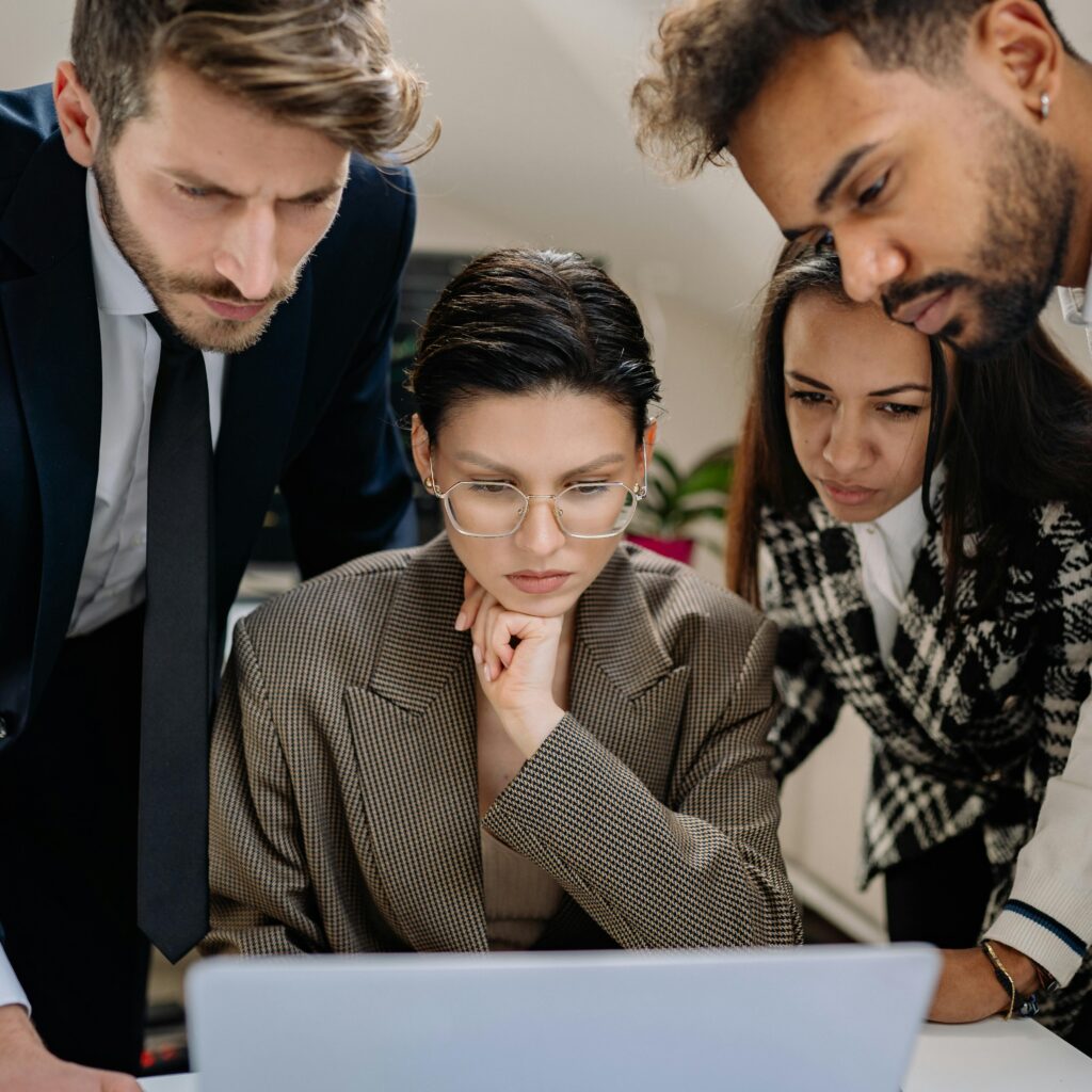 A diverse group of people gathered around a laptop, watching something together with curiosity