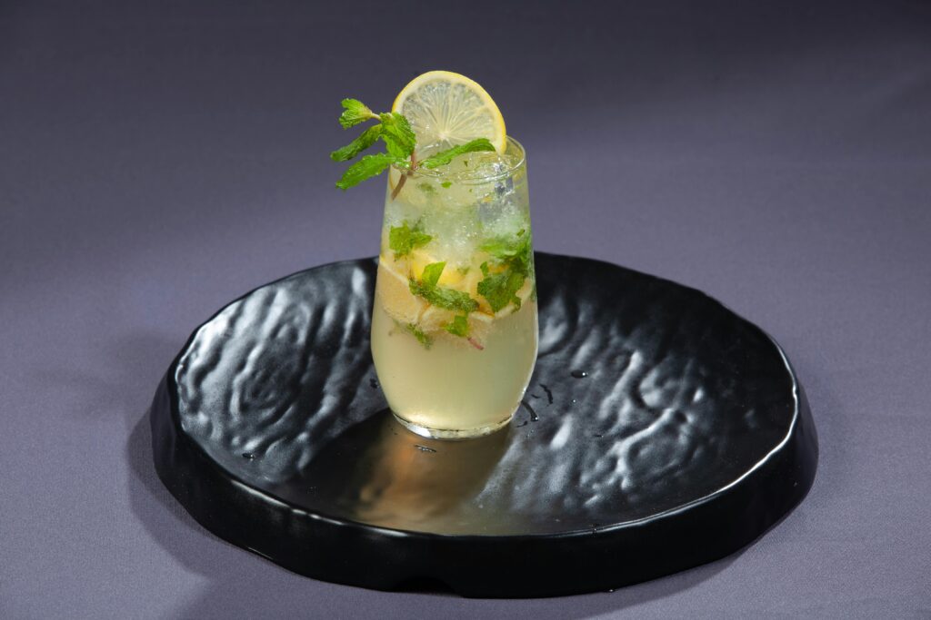 A chilled lemon and mint drink served on a textured black plate, highlighting summer refreshment. Mentha leaves with a glass of mint juice, ideal for summer refreshment with watermelon