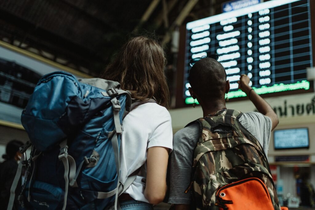 pexels-photo-4907611-4907611 Two backpackers checking the digital board at a train station for travel information.
